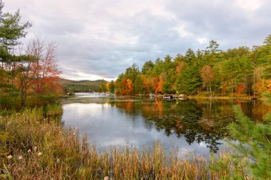 Sürat tekneleri, sonbahar mevsiminde bir dağ gölünün ormanlı kıyıları boyunca yelkenlilere demirlediler. Adirondacks, New York, ABD.