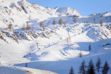 Açık bir kış gününde Alplerdeki bir kayak merkezinde kayak asansörüne binen kayakçılar. Dolomitler, İtalya.