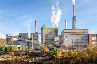 Factory with smoking chimneys on a the bank of a river on a sunny autumn day. Rumford, ME, USA. clipart