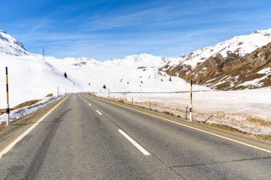Issız dağ geçidi yolu güneşli bir günde karla kaplı zirvelerle çevrili. Julier Geçidi, İsviçre.