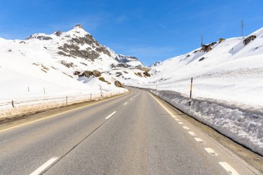 Mavi gökyüzünün altındaki karlı bir dağ manzarasında terk edilmiş viraj yolu. Julier Geçidi, İsviçre.