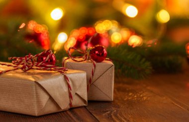 Close up of two wrapped Christmas gifts on a rustic wooden table with colourful defocused decorations and lights in background clipart