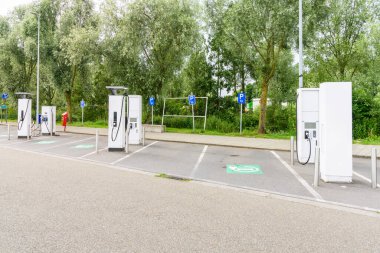 Bulutlu bir yaz gününde Belçika 'da bir otoyolun servis alanında elektrikli arabaların şarj noktaları boş.