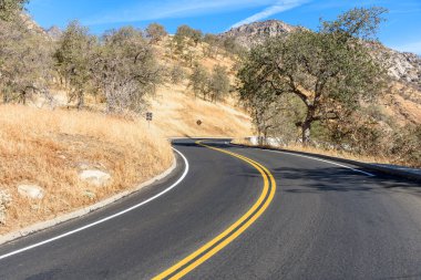 Kaliforniya Sierra Nevada 'da, güneşli bir sonbahar gününde mavi gökyüzünün altında boş kıvrımlı bir dağ yolu.