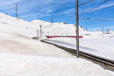 Güneşli bir günde İsviçre Alplerinde karlı yüksek bir dağ geçidinden geçen kırmızı yolcu treni. Bernina Geçidi, İsviçre.