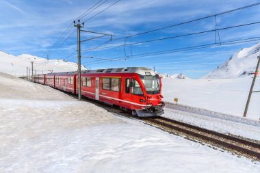 Güneşli bir günde, mavi gökyüzünün altında, karlı bir dağ manzarasında, tek bir raydan geçen kırmızı yolcu treni. Bernina Geçidi, İsviçre.