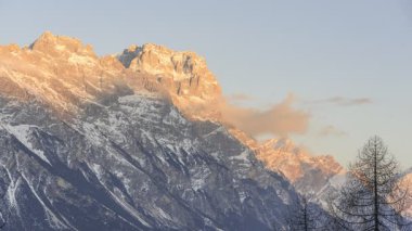 Kışın günbatımında Dolomitlerin içinde karlı bir dağın tepelerinde dönen bulutlar - zaman aşımı