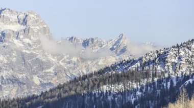 Kış mevsiminde Dolomitler 'de karla kaplı görkemli bir kayalık zirvede hareket eden bulutlar.