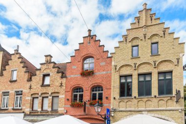 Parçalı bulutlu bir yaz gününde eski bir şehir merkezindeki tarihi şehir evlerinin alçak açılı görüntüsü. Ypres, Belçika.