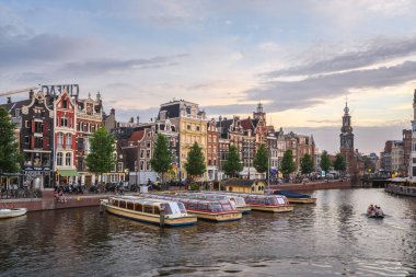 Amsterdam, Hollanda - 23 Haziran 2022: Alacakaranlıkta Amstel Caddesi boyunca geleneksel mimari. Munt Kulesi uzaktan görülebilir. Amstel Nehri boyunca uzanan Amstel Caddesi, Amsterdam 'ın en güzel caddelerinden biridir..