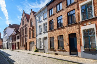 Güneşli bir yaz gününde tarihi bir şehir merkezinde, kaldırımlı bir cadde boyunca yenilenmiş tuğla kasaba evleri. Bruges, Belçika.