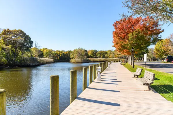 Terk edilmiş ahşap kaldırımlar açık bir sonbahar gününde nehir limanı boyunca uzanan banklar ve renkli ağaçlarla kaplı. Riverhead, Long Island, New York, ABD.