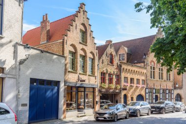 Güneşli bir yaz gününde şehir merkezindeki kaldırımlı bir cadde boyunca geleneksel tuğlalı evler ve dükkanlar. Bruges, Belçika.