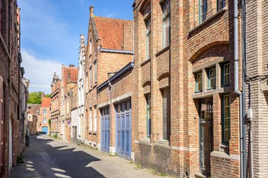 Güneşli bir yaz gününde şehir merkezinde dar kaldırımlı bir cadde boyunca eski tuğlalı evler. Bruges, Belçika.
