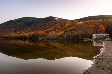 Sonbahar yapraklarının zirvesinde ormanlık bir dağ alacakaranlıkta sakin bir gölün sularına yansıyor. Echo Gölü, Franconia Notch, NH, ABD