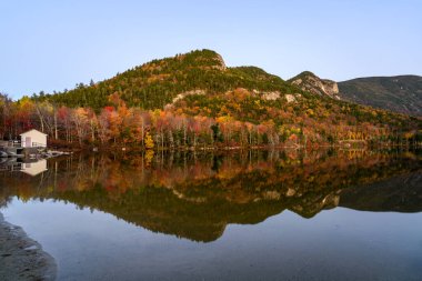 Alacakaranlıkta sonbahar renklerinin zirvesinde orman kıyıları olan dağ gölü. Sudaki yansıma Echo Gölü, Franconia Notch, NH, ABD.