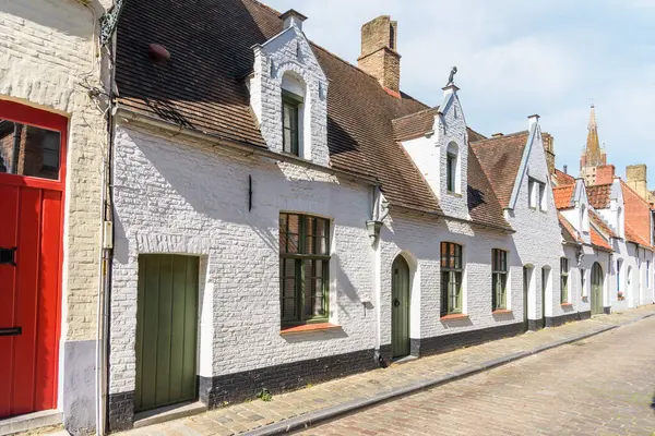 Güneşli bir yaz gününde eski bir şehir merkezinde, kaldırımlı bir cadde boyunca uzanan tarihi teraslı kulübeler. Bruges, Belçika.