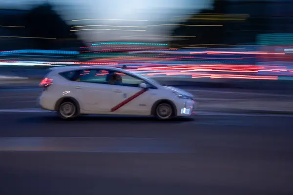 Madrid taksisinin hareketli görüntüsü alacakaranlıkta trafiğin yoğun olduğu bir caddede ilerliyor ve arka plan aydınlatma tarzıyla bulanıklaşıyor.