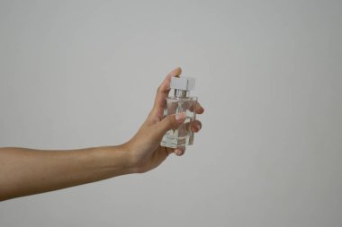 Beyaz arka planda bir şişe parfüm tutan bir kadın.