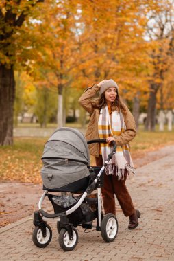 Genç bir anne bir bebek arabası ile sonbahar parkta yürüyor. Bir çam ormanı içinde açık havada bir bebek ile yürüme. Yeni doğan, Aile, çocuk, ebeveynlik.