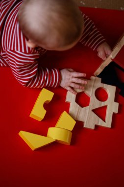 Bebek, kırmızı arka planda geometrik şekillerle sınıflandırıcı mantık oyunları oynuyor. Mutlu çocuk oyuncak eviyle oynuyor, mantık öğreniyor..