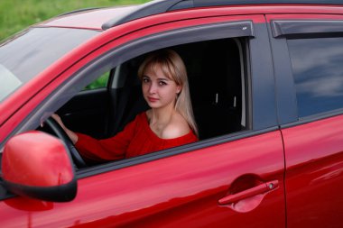 Genç, çekici sarışın kız yeni kırmızı araba içinde gülümseyen ve seyir hayatını memnun