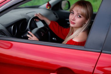 Genç, çekici sarışın kız yeni kırmızı araba içinde gülümseyen ve seyir hayatını memnun