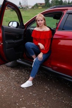 Genç, çekici sarışın kız yeni kırmızı araba içinde gülümseyen ve seyir hayatını memnun