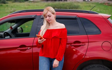 Gülümseyen, mutlu, iyimser, güzel bir kadının resmi. Plajda arabanın yanında cep telefonuyla sohbet eden kırmızı bir kadın..