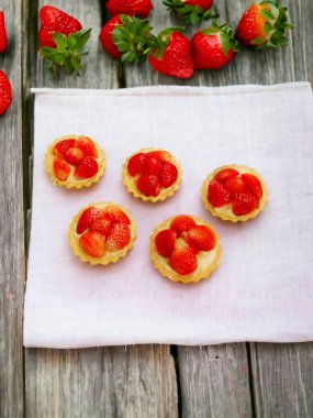 Bir grup küçük hamur işi, pastel renkli bir masada çilekli, arka planda ahşap bir çit var.