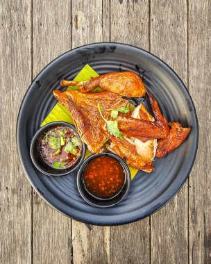 Siyah bir tabakta servis edilen ızgara tavuk, soslu ve ahşap masada garnitür..