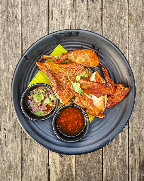 Siyah bir tabakta servis edilen ızgara tavuk, soslu ve ahşap masada garnitür..