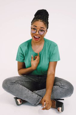 Mutlu Afrikalı Amerikalı kadın kendini göstererek yerde oturuyor. Gri arka planda gülümseyen harika siyahi kızın stüdyo çekimi..