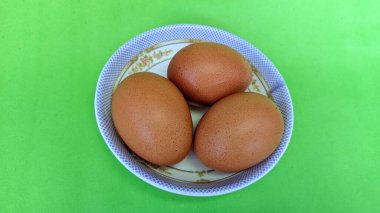 Yeşil arka planda izole edilmiş bir tabakta çiğ kahverengi yumurta manzarası. Yumurta pişirmede yaygın bir malzemedir. Yumurta proteini etkili bir şekilde emilir. Yiyecek konsepti.