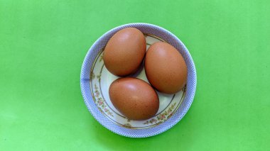 Yeşil arka planda izole edilmiş bir tabakta çiğ kahverengi yumurta manzarası. Yumurta pişirmede yaygın bir malzemedir. Yumurta proteini etkili bir şekilde emilir. Yiyecek konsepti.