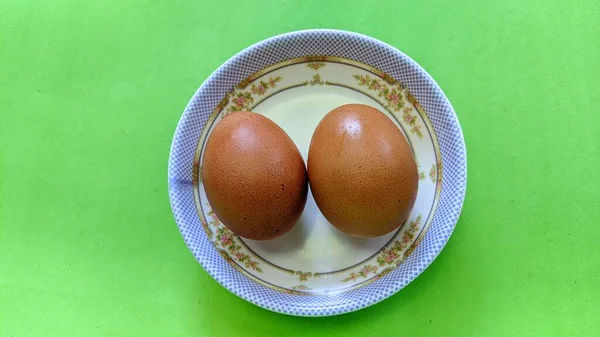 緑の背景に隔離されたプレート上の2つの生の茶色の卵のトップビュー 卵は料理によく使われる食材です 卵タンパク質は効率的に吸収できるタンパク質である 食のコンセプト — ストック写真