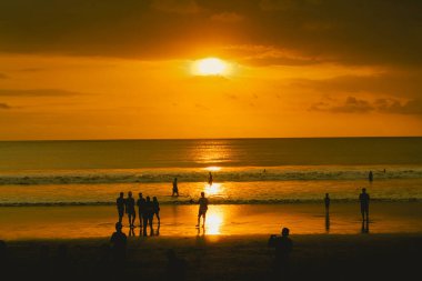 Sahilde gün batımında insan siluetleri. Gökyüzü altın gibi. Güneş ışığının turuncu yansıması.