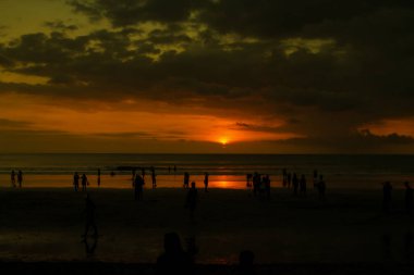 Sahilde gün batımında insan siluetleri. Gökyüzü altın gibi.