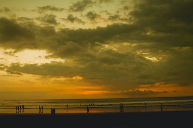 Sahilde gün batımında insan siluetleri. Gökyüzü altın gibi.