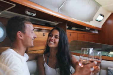Genç bir çift yelkenli teknede tatil yaparken bir bardak şarabın tadını çıkarıyor.