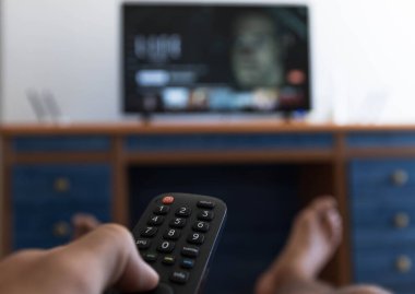 Uzaktan kumandayla TV 'de ayakları masaya çarpan bir dizi ararken.