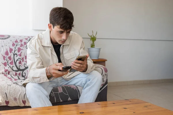 Bir film ararken cep telefonunu tutan genç adam ve diğer elinde uzaktan kumanda var..