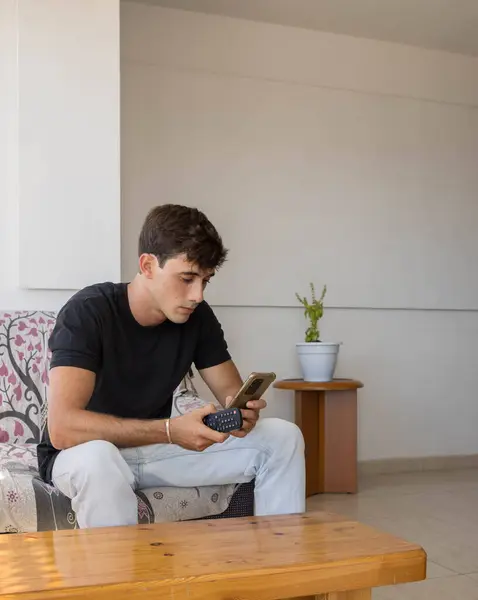 Kanepede oturan bir gencin dikey fotoğrafı. Cep telefonuna bakıp hangi filmi izlediğini görmek için..