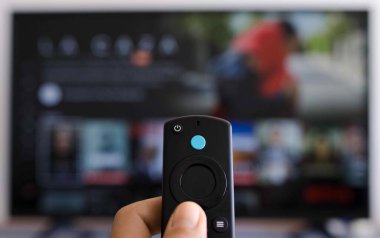 Akıllı televizyondan modern bir uzaktan kumandayı tutan bir elin fotoğrafı.