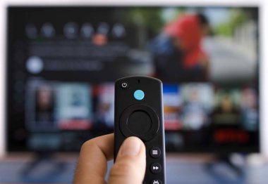 Akıllı televizyondan modern bir uzaktan kumandayı tutan bir elin fotoğrafı.