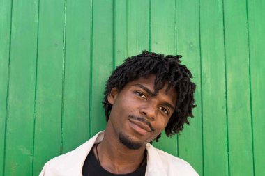 Afro saçlı genç bir çocuk kameraya bakıyor. Yeşil arkaplan