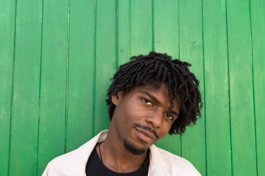 Afro saçlı genç bir çocuk kameraya bakıyor. Yeşil arkaplan