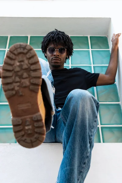 窓に座ったアフロ少年が足でカメラにぶつかった 縦の写真 — ストック写真
