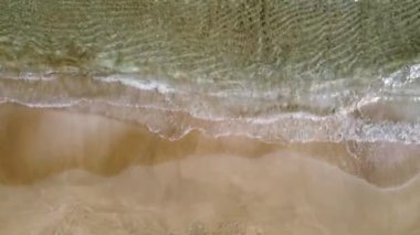 Deniz dalgaları kumlu sahil şeridinde dalgalanırken hiç bitmeyen güzel ve kusursuz görüntülerin drone görüntüsü. Altın plajın, derin mavi okyanus suyu ve köpüklü dalgalarla buluşmasının havadan çekimi. 4k görüntü