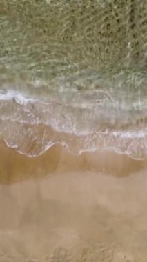 Deniz dalgaları kumlu sahil şeridinde dalgalanırken hiç bitmeyen güzel ve kusursuz görüntülerin drone görüntüsü. Golden Beach 'in derin mavi suyla buluşmasının dikey görüntüsü. 4k görüntü